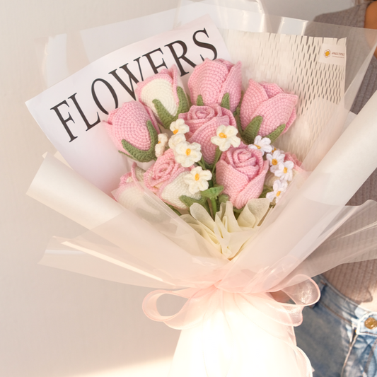 Bouquet of pink knitted flowers with a newspaper labeled 'FLOWERS' in the background.