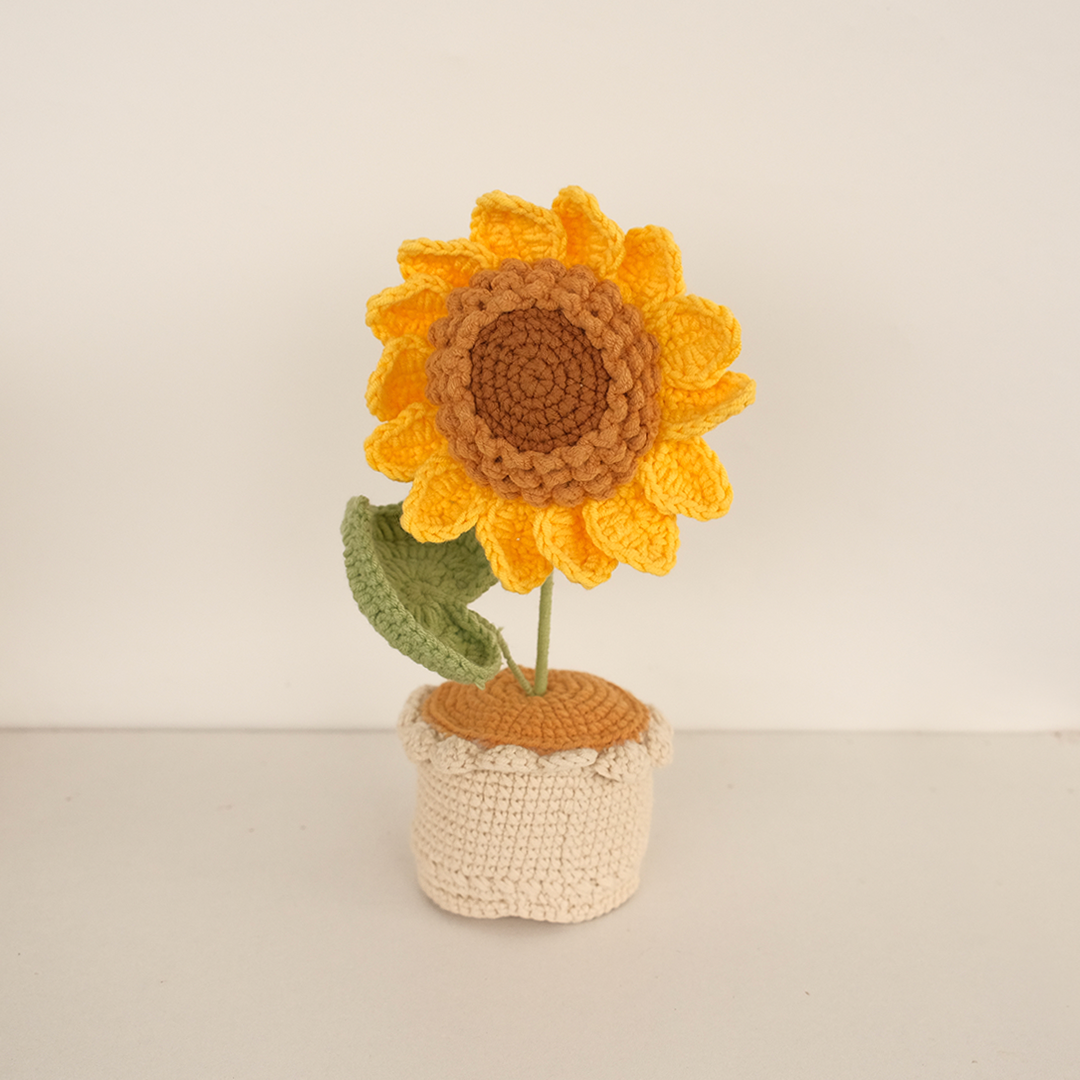 A crocheted sunflower pot with a yellow sunflower in a beige pot, placed against a white background.